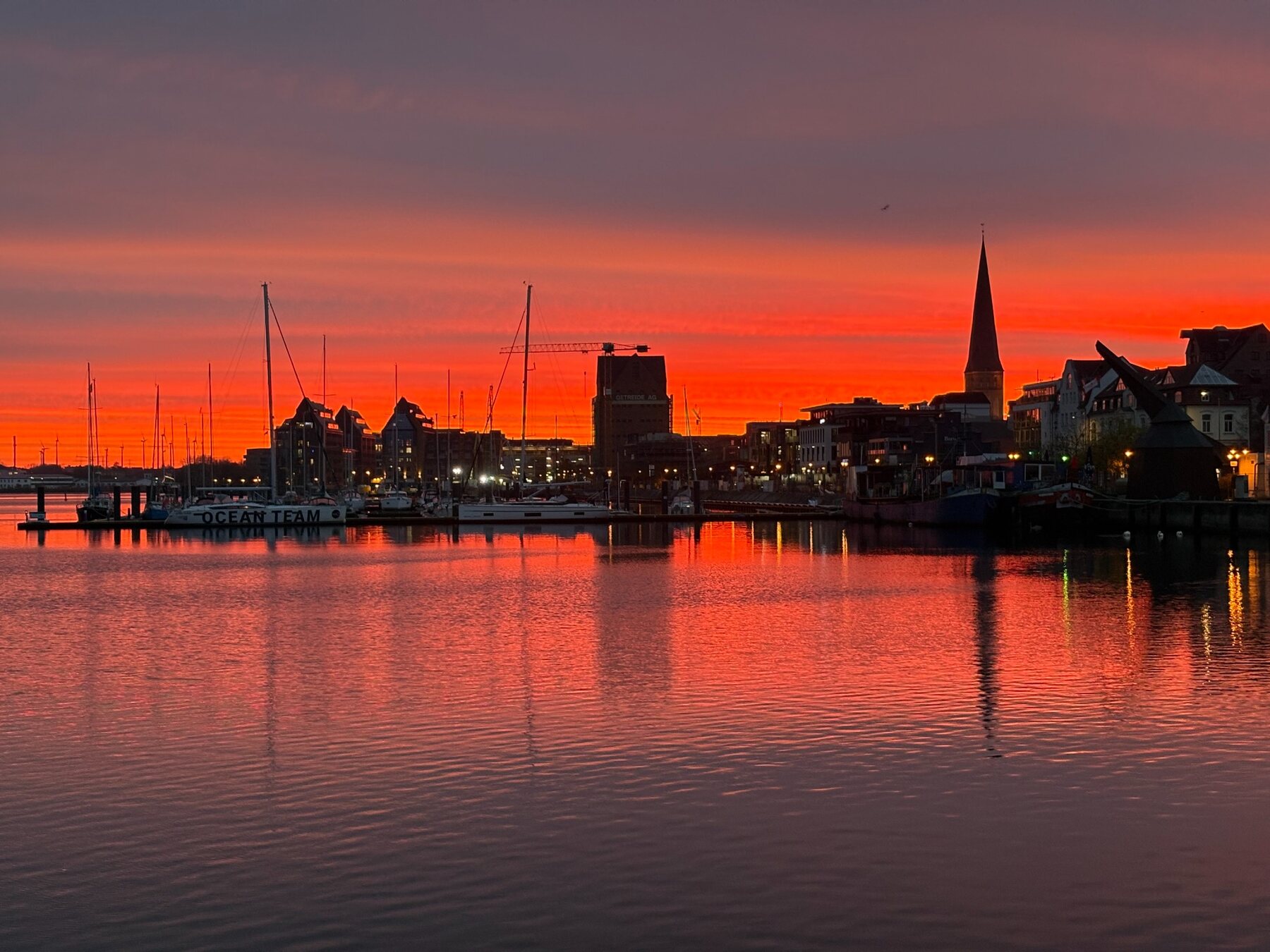 Rostocker Stadthafen mit Booten und Kirchturm unter einem tiefroten Abendhimmel